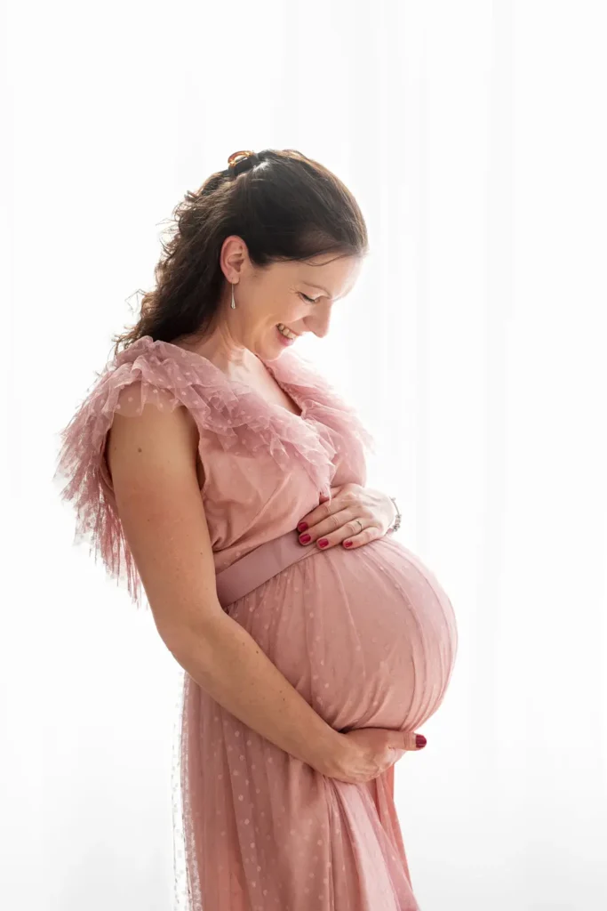 Femme enceinte qui tient et regarde son ventre tendrement dans un fond lumineux