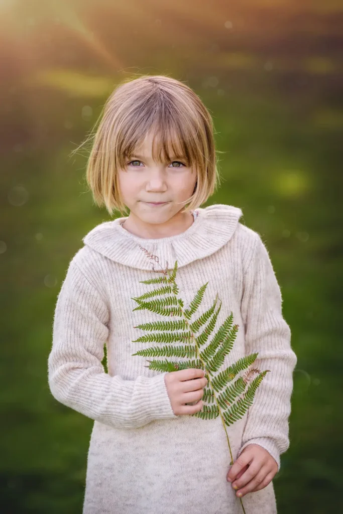 Petite fille dans l'herbe tenant une feuille sous une lumière douce.