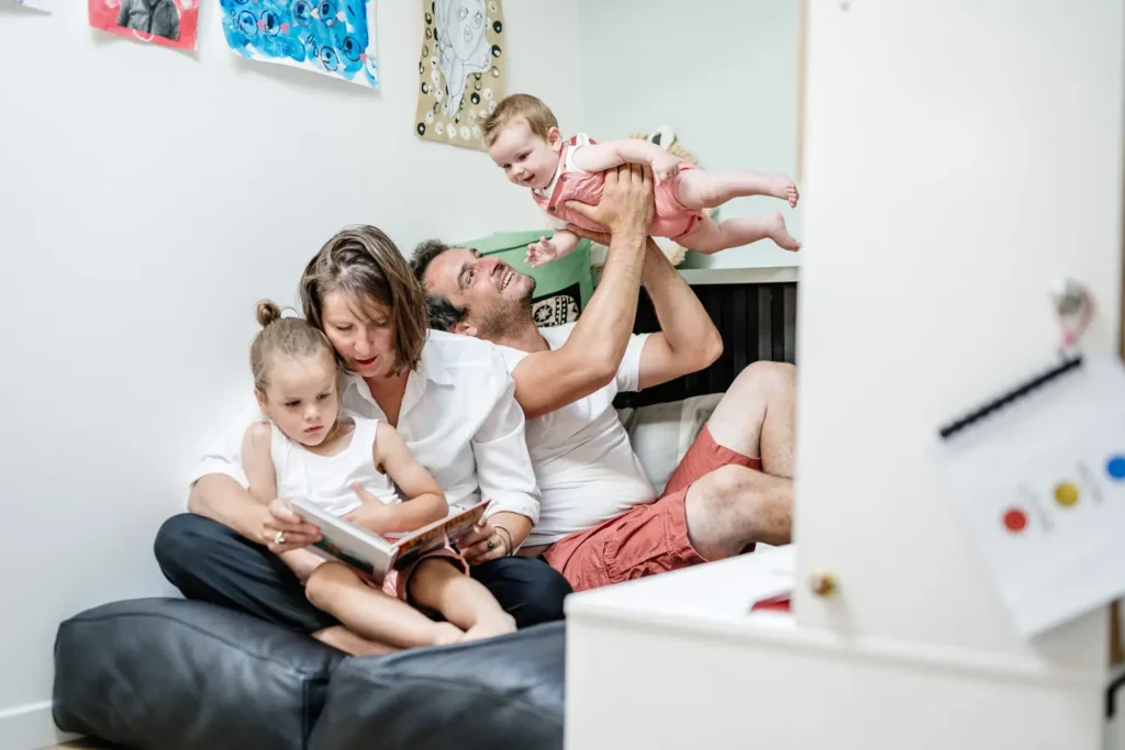 Mère qui lit un livre et le père porte bébé dans les airs.