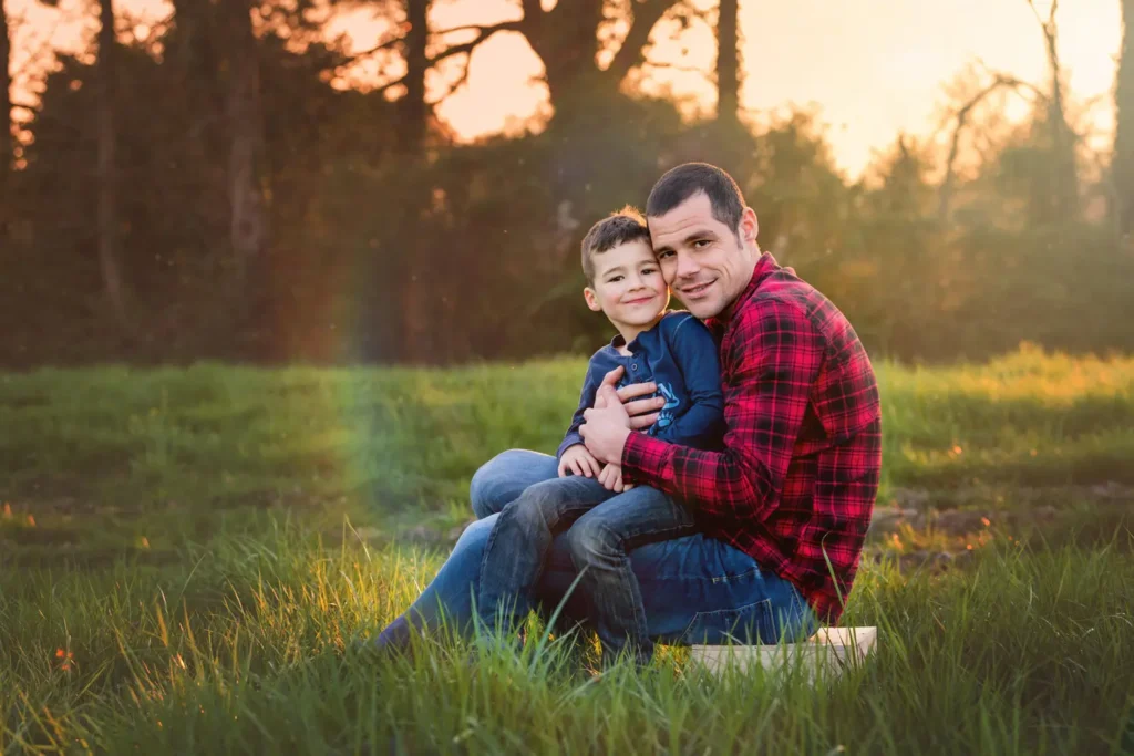 Père et son enfant assis dans l'herbe se faisant un câlin