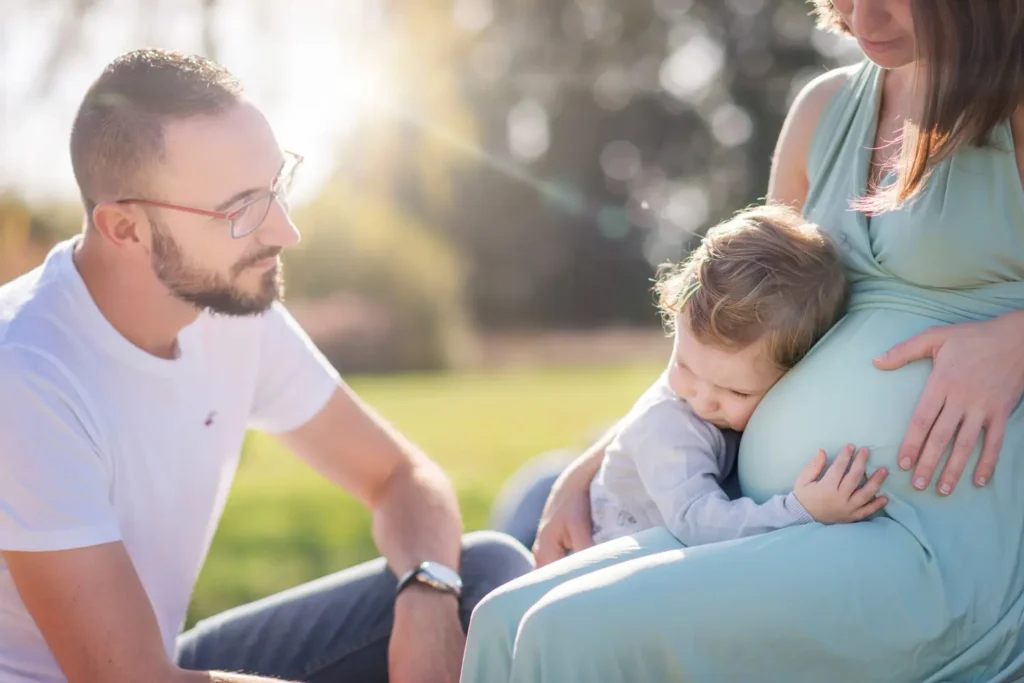 Enfant qui fait un câlin au ventre de sa mère sous le regard de son père