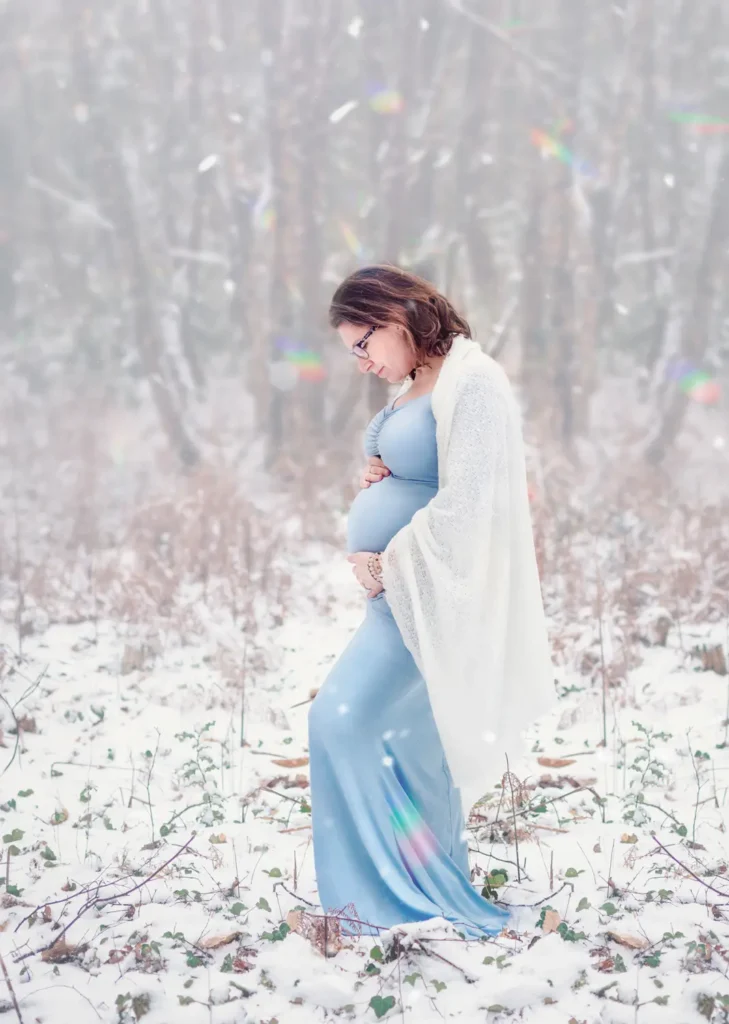 Femme enceinte dans une longue robe qui regarde et tient son ventre dans la neige