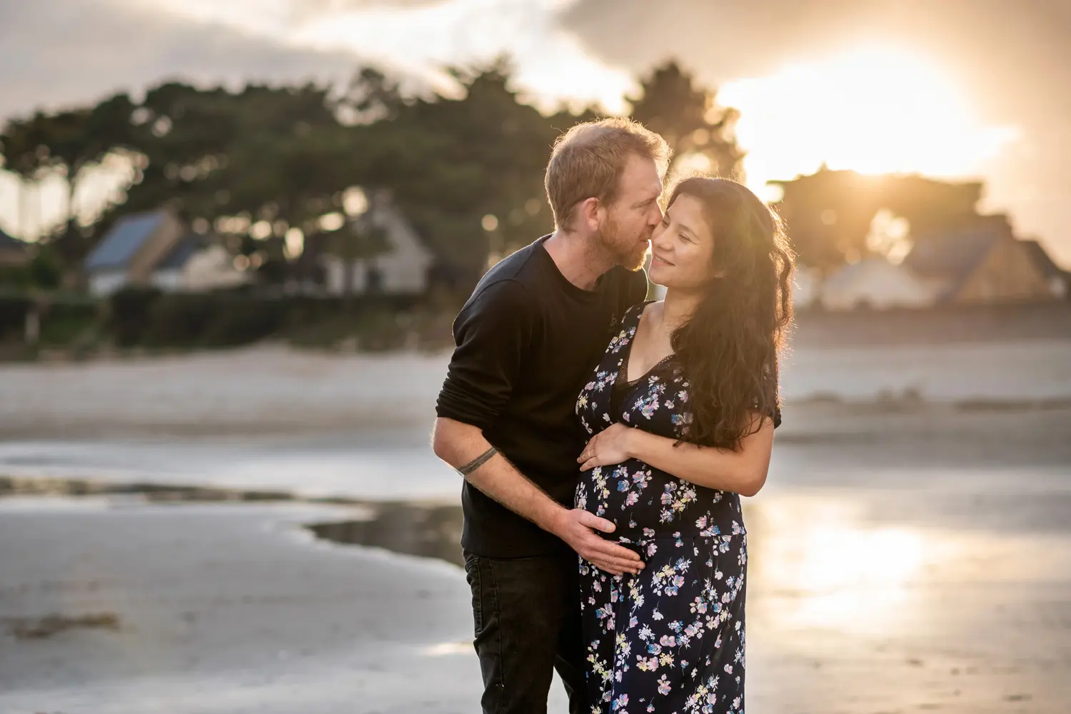 Maman enceinte et le papa qui tiennent le ventre sous un coucher de soleil à la plage