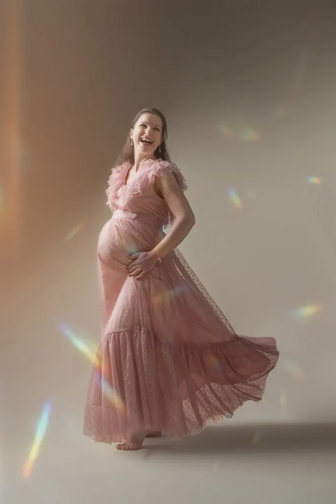 Maman enceinte avec une longue robe en mouvement qui tient son ventre en rigolant