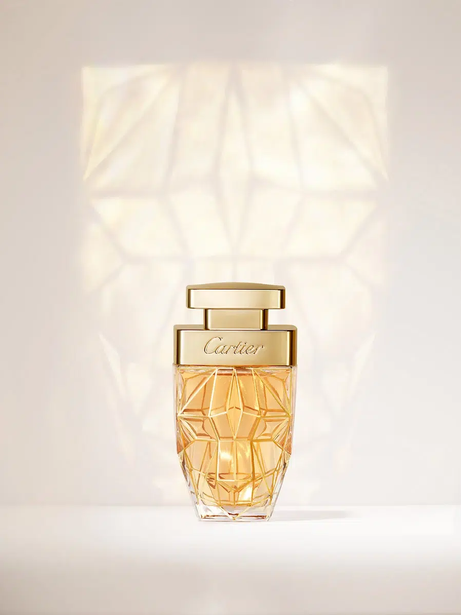 Bouteille de parfum sur fond blanc avec son reflet visible à l’arrière.